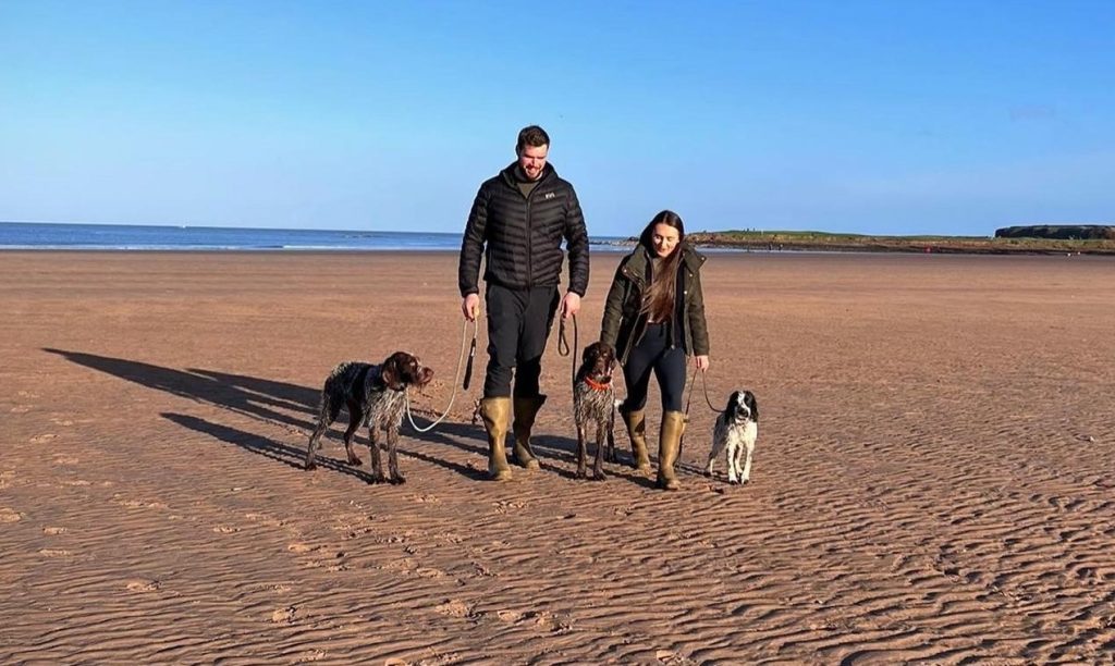 Quintin, Bethan and their dogs walking on the beach.